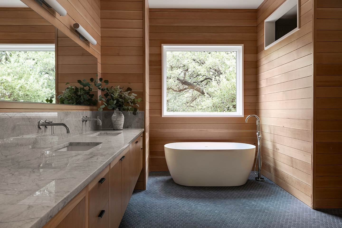 Primary bath with a freestanding tub, wood ceiling and a window onto oak trees