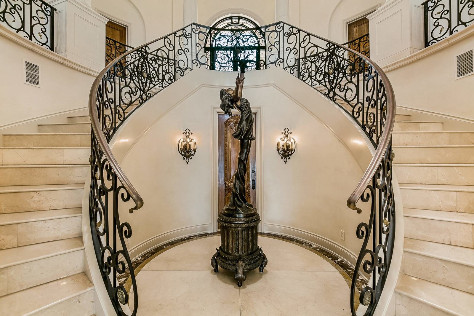 Grand curved staircase with wrought-iron railing and a statue