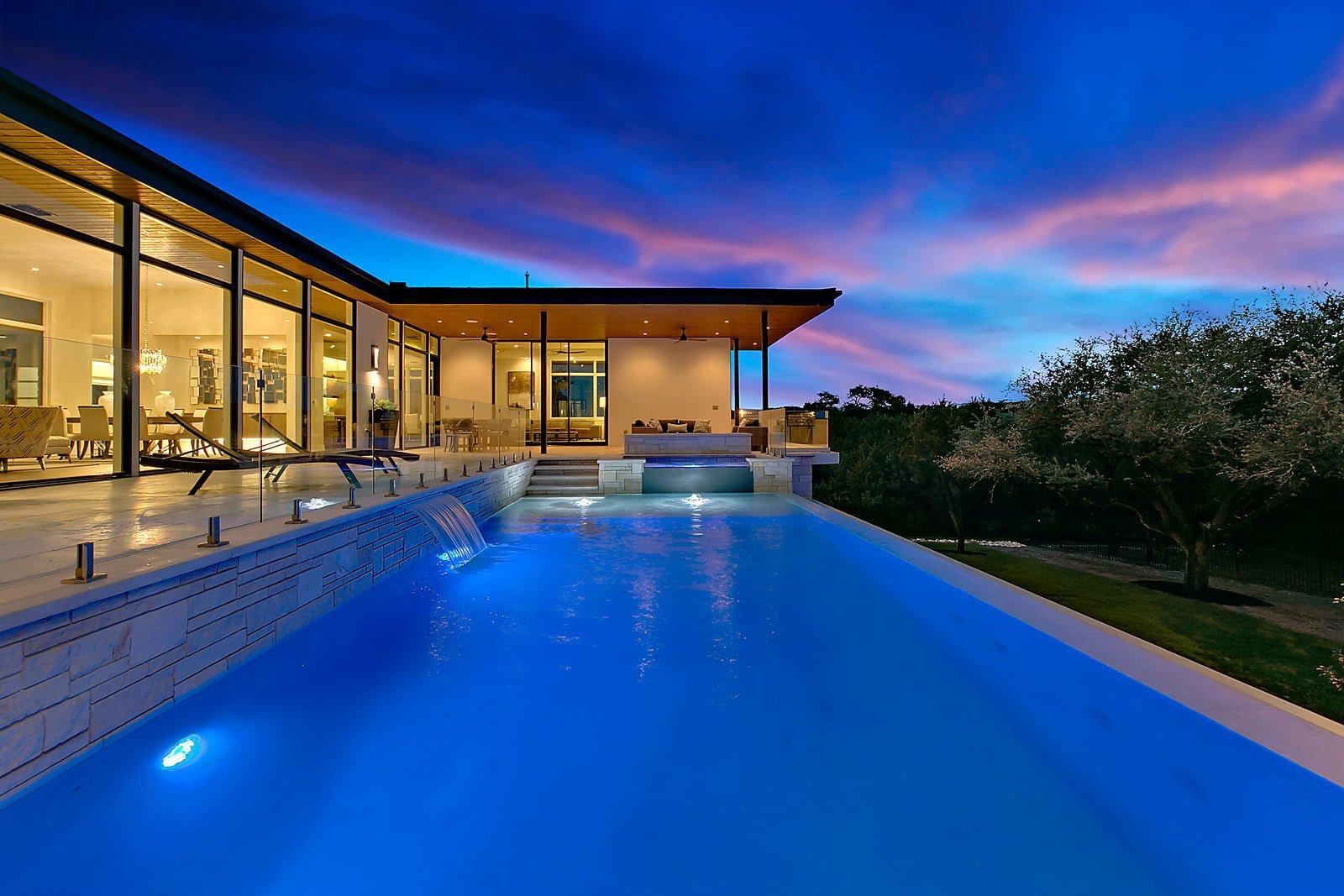Infinity pool at twilight beside a glass-walled modern home
