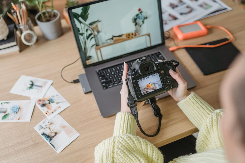 Photographer adjusts camera settings while reviewing images on laptop in a creative workspace